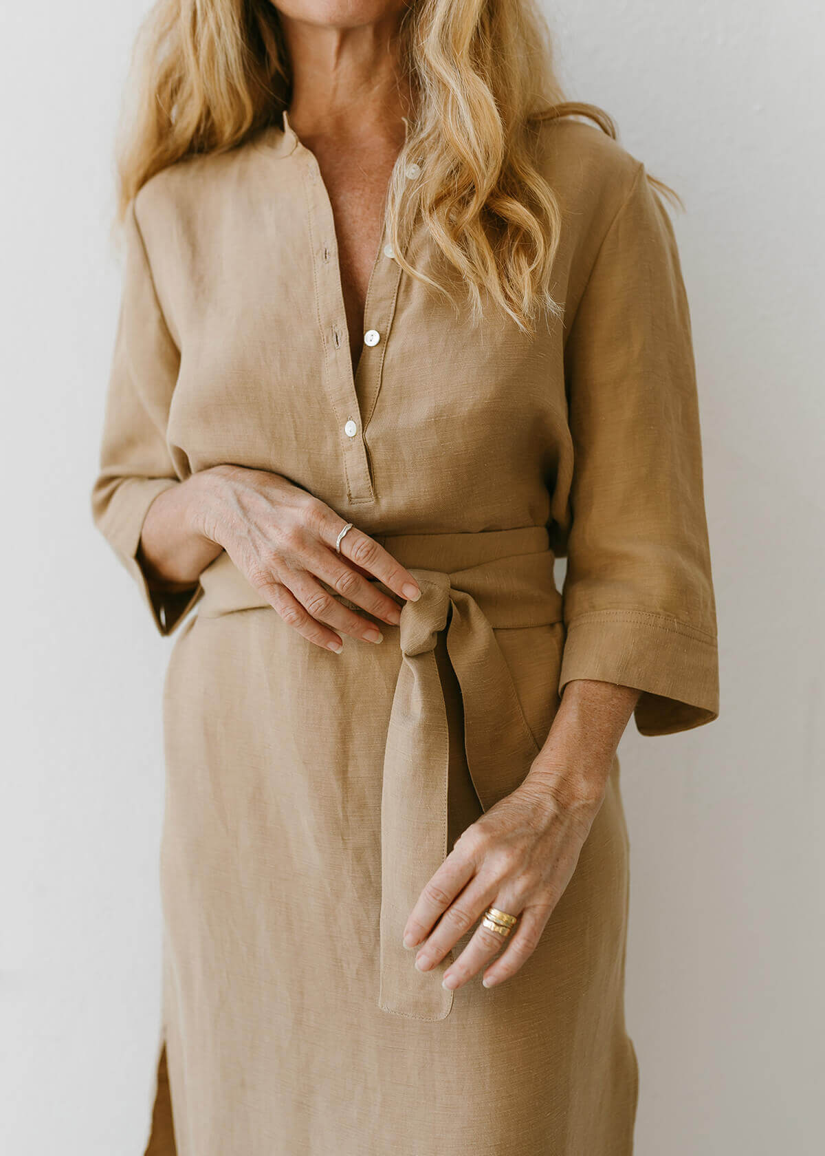 Woman wearing a Tunic style dress with pockets, a detached belt and high side slits, in a light brown camel color..