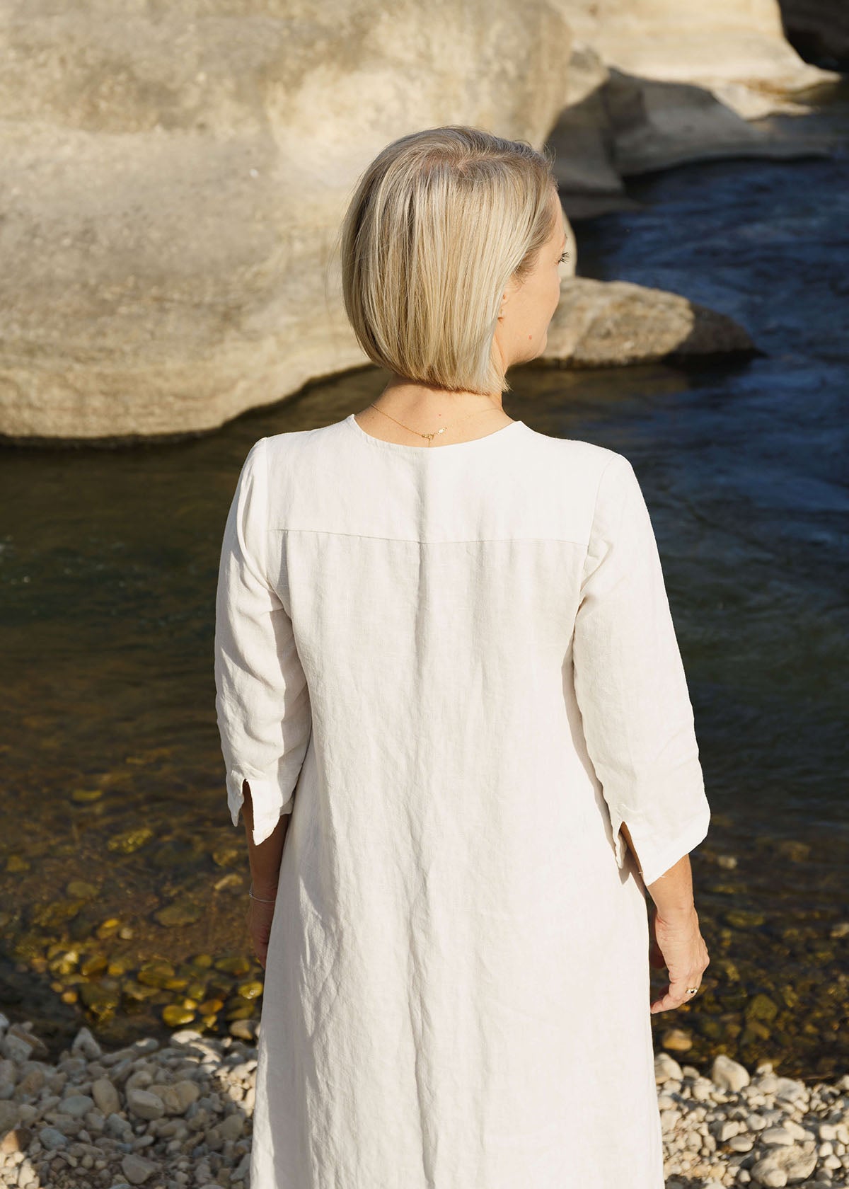 Back view of a woman wearing the Sienna everyday buttoned shirtdress in white, with ¾ sleeves, a V-neck, an uneven hemline.