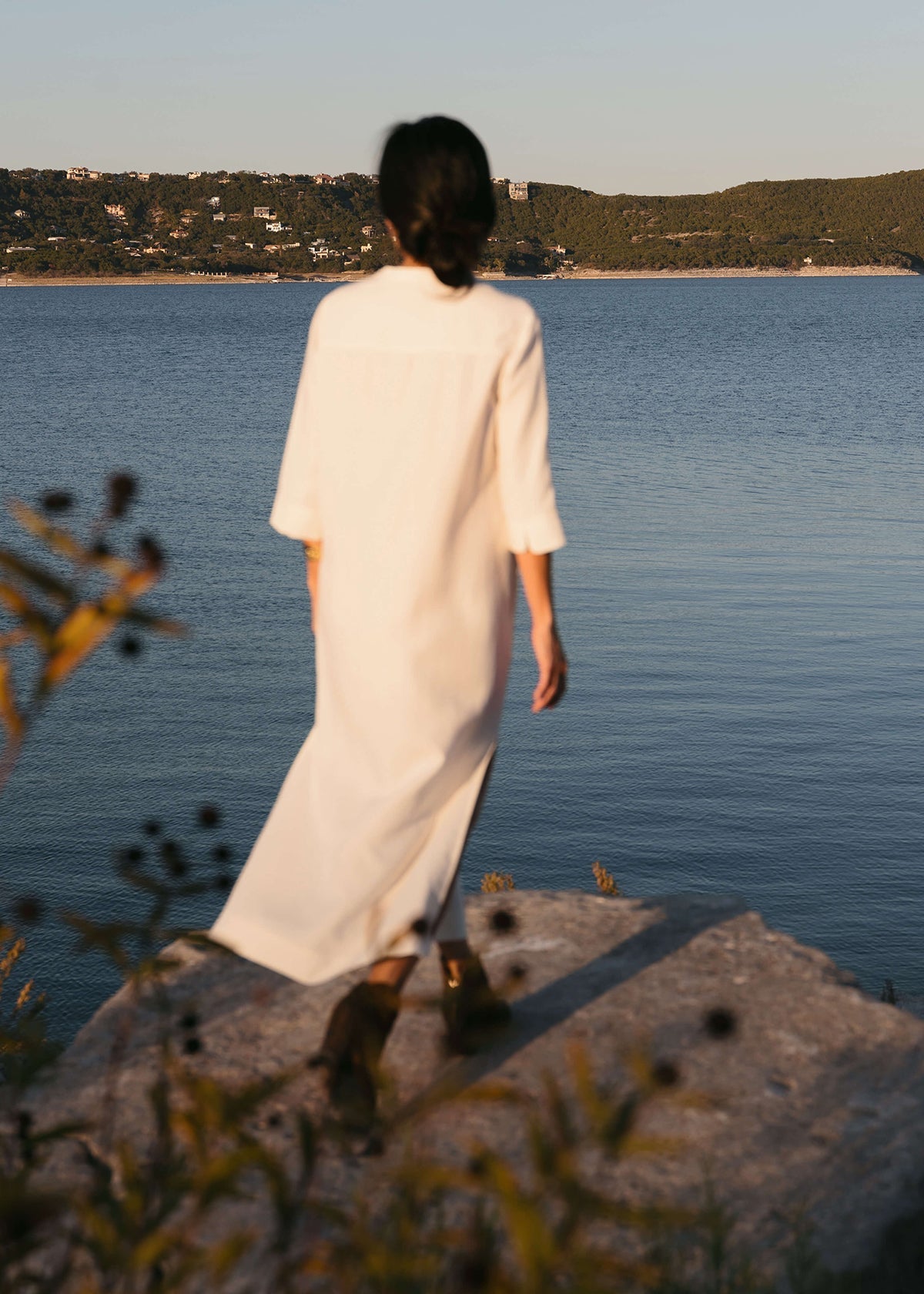 Back view of a Woman wearing a Tunic style dress with pockets, and high side slits, in white.
