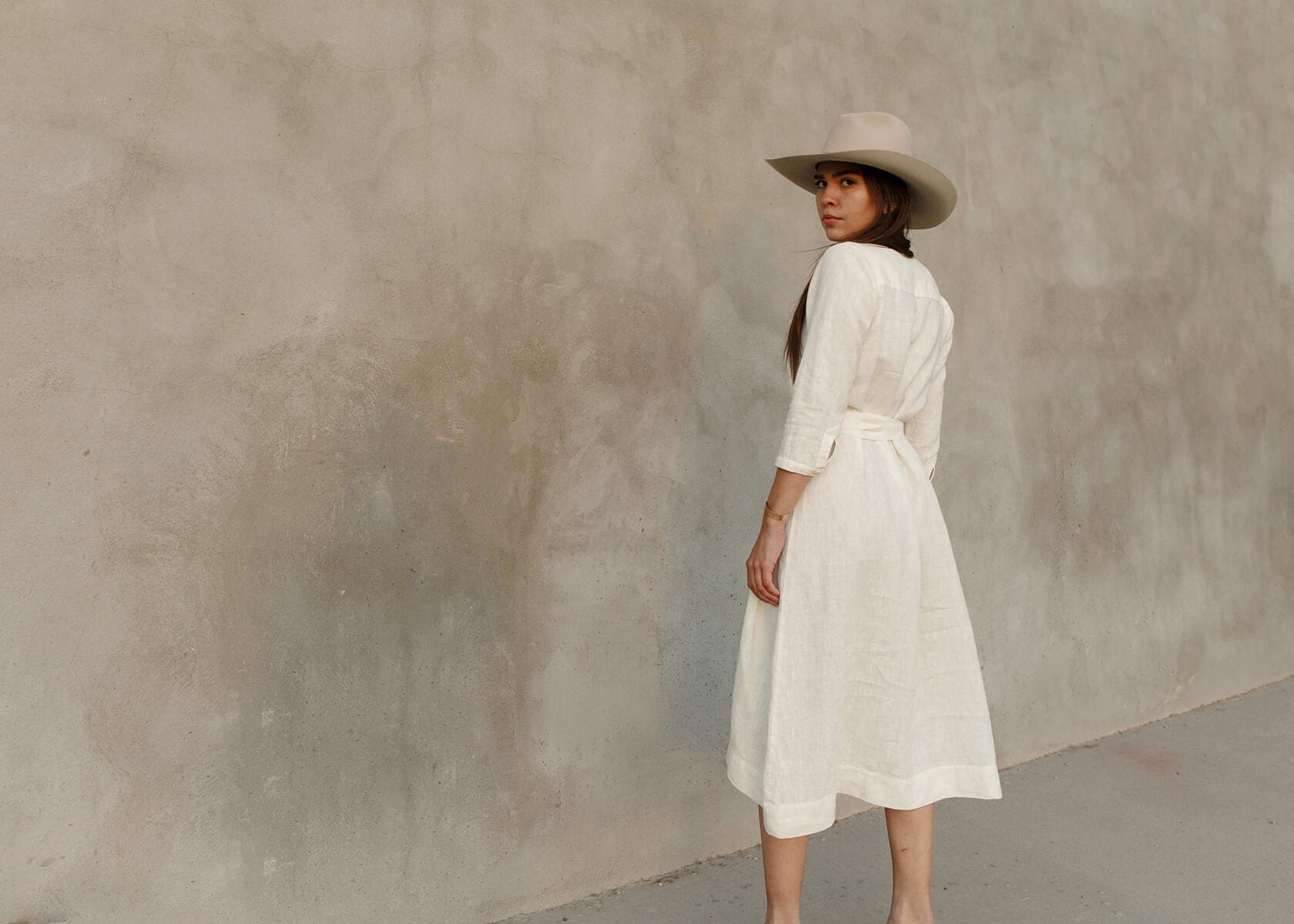 Woman wearing a Tunic style dress with pockets, a detached belt and high side slits, in a light brown camel color..