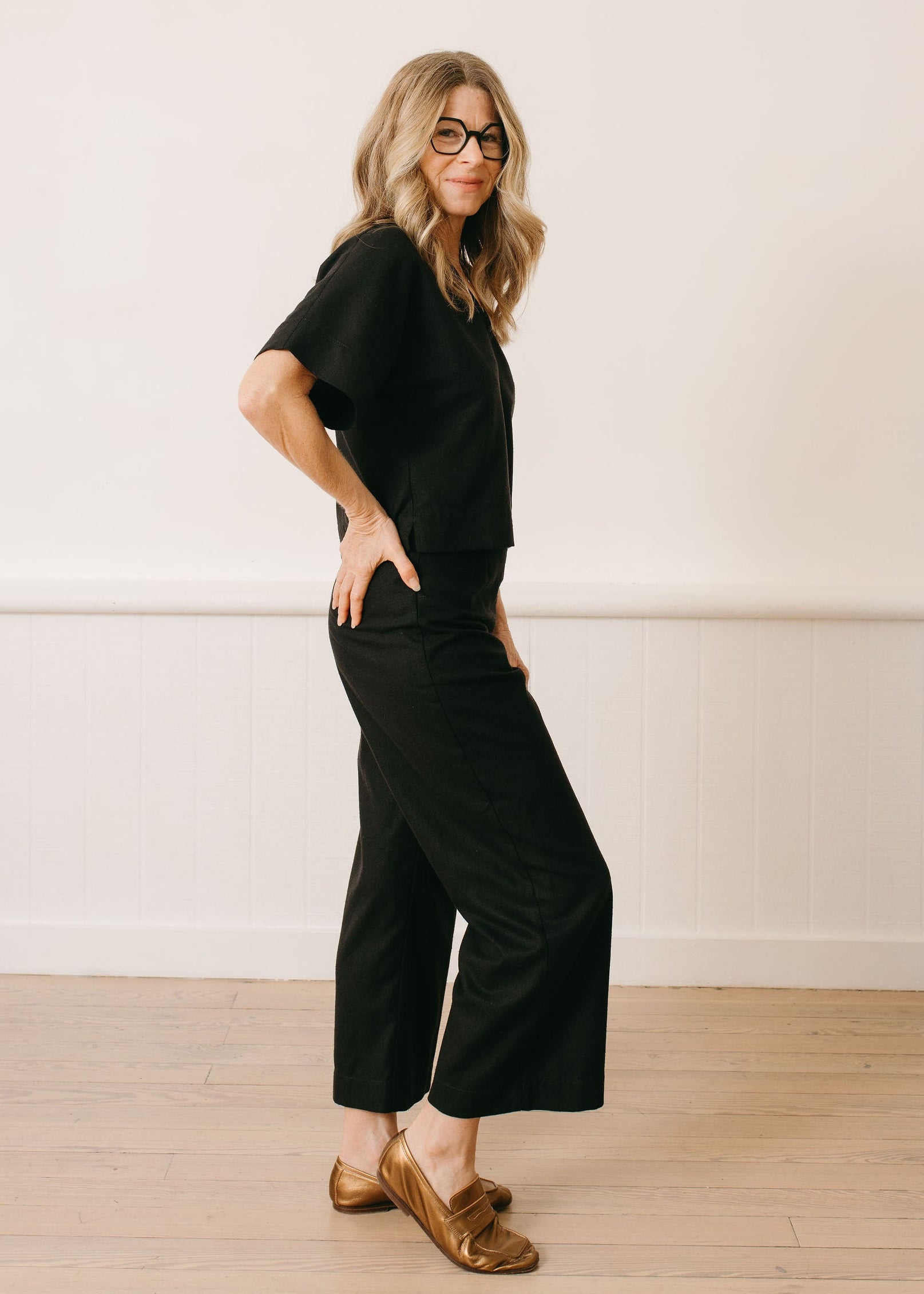Woman wearing a black outfit standing against a white wall.
