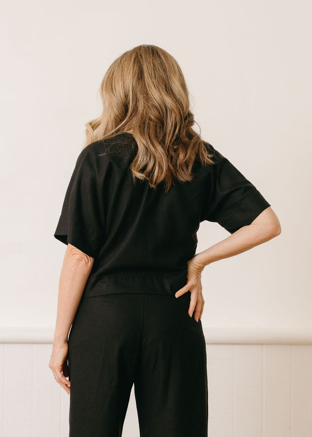 Woman wearing a black outfit standing against a white wall.