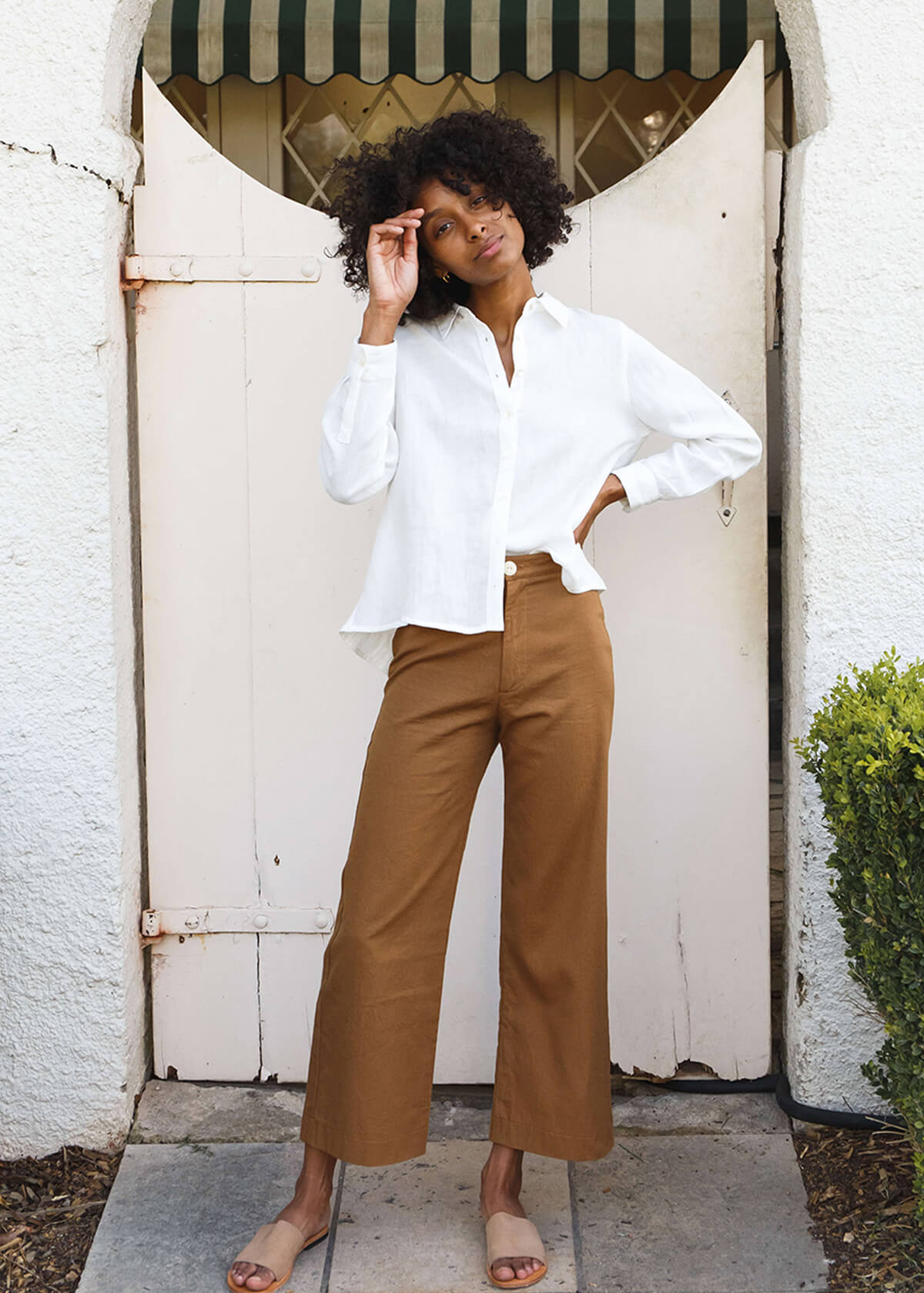woman wearing brown high-waisted, wide-leg pants with a slight ankle crop, single button front closure, and back pockets.